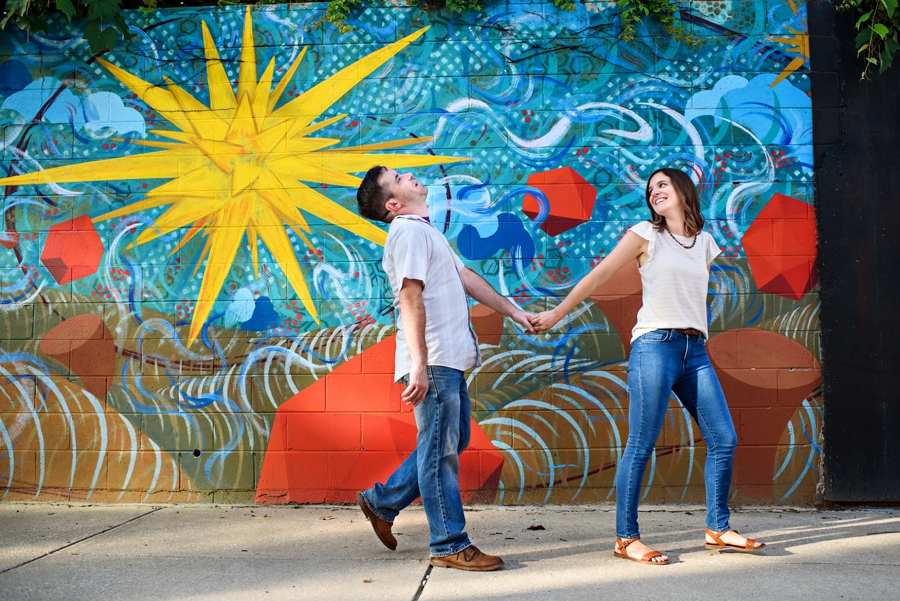 A fun couple walk in front of a grafiti wall in their fishtown engagement session.